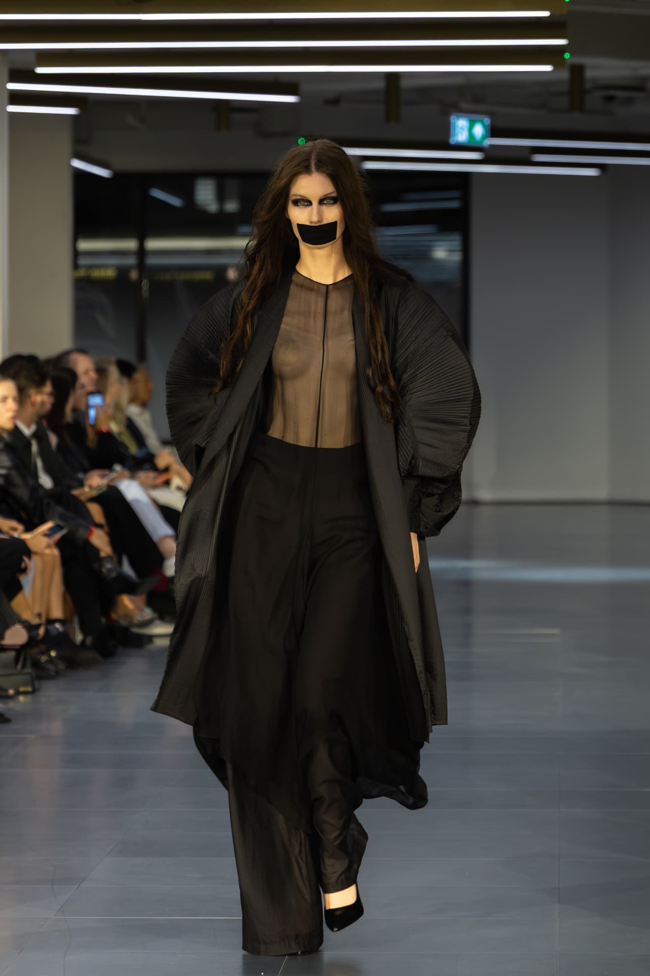 Model in a sheer black coat and wide-leg trousers