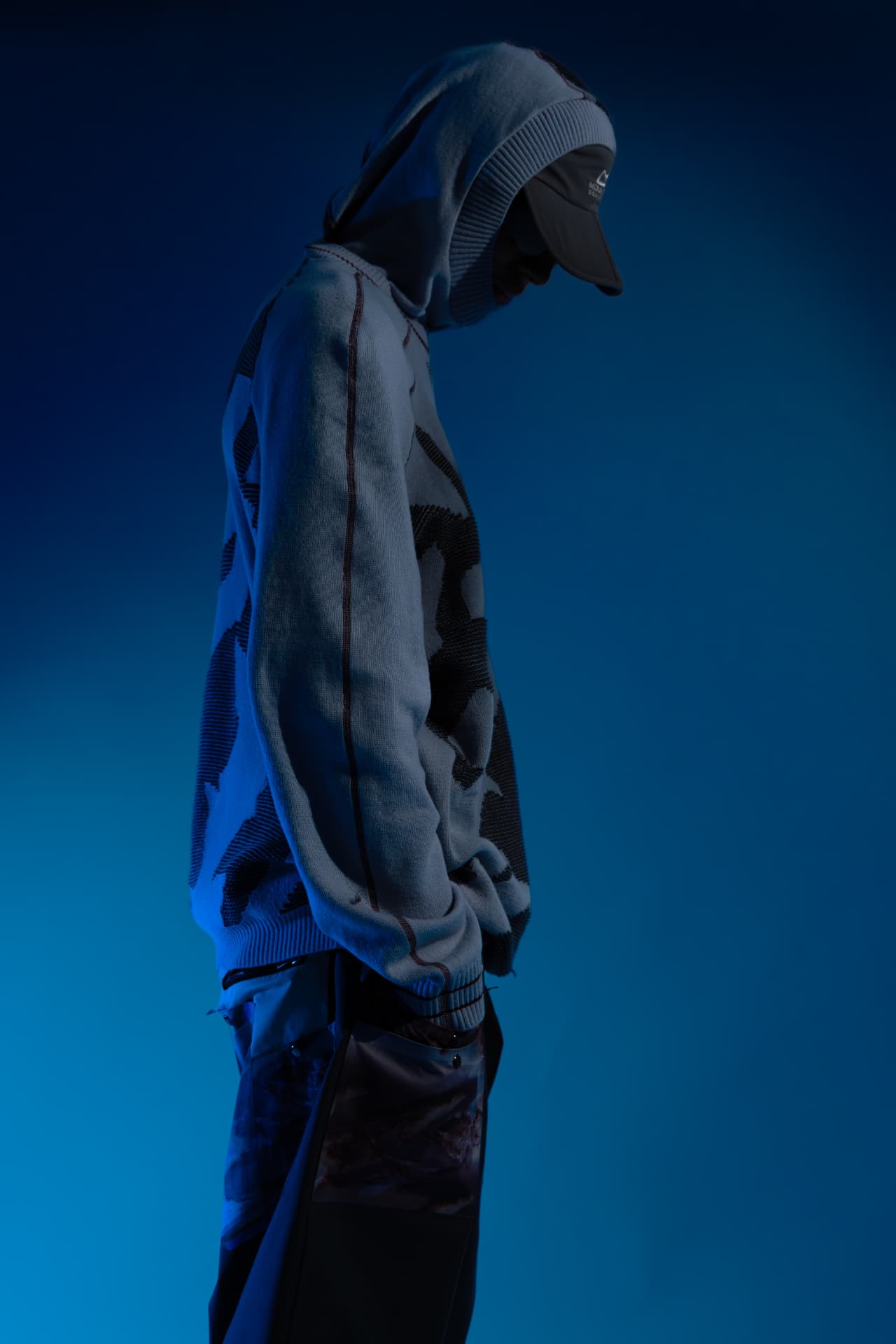 Side profile of a hooded knit and cap under blue light