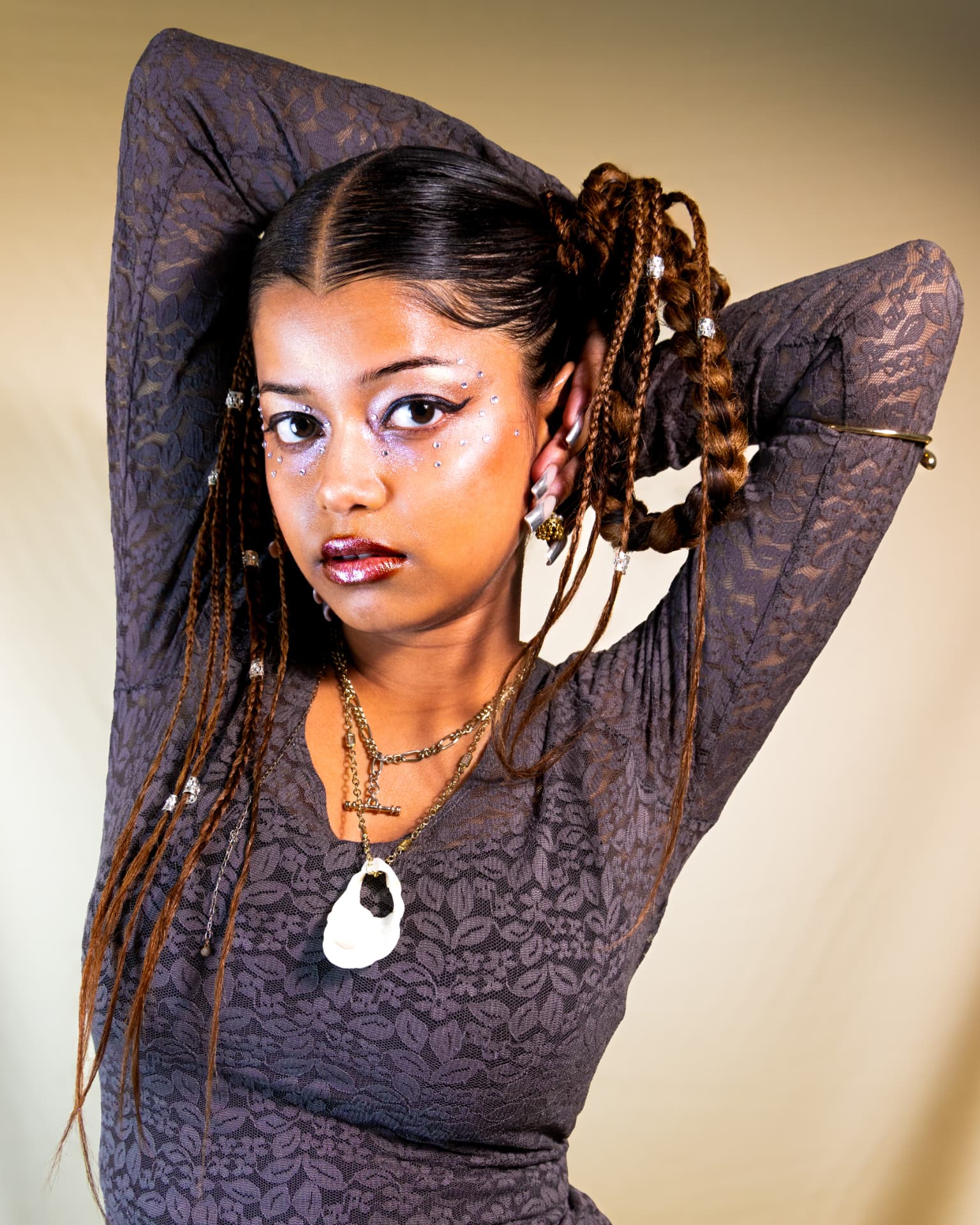 Model standing with arms raised, braided hair and crystal makeup