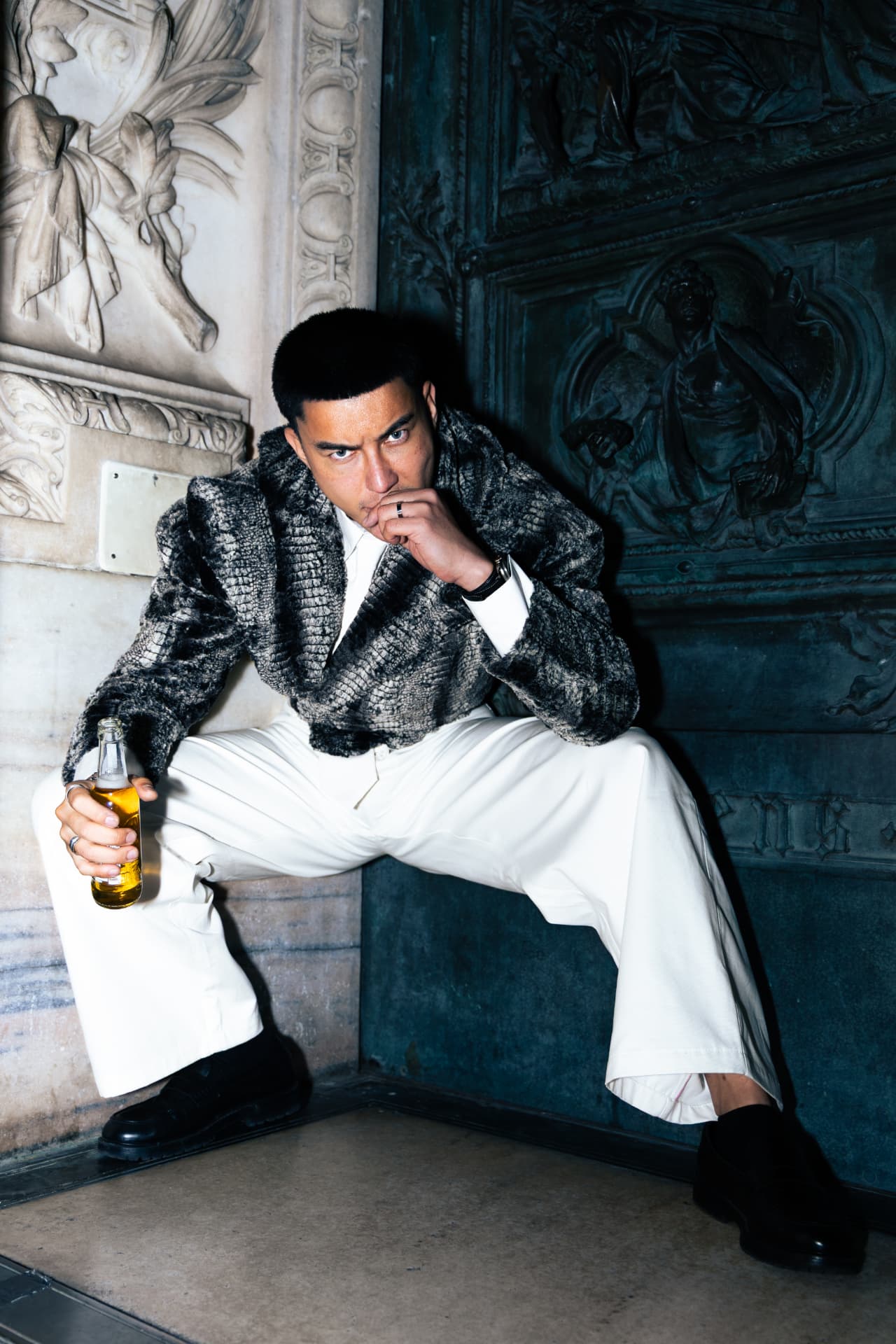 Model crouched in a grey fur jacket holding a bottle