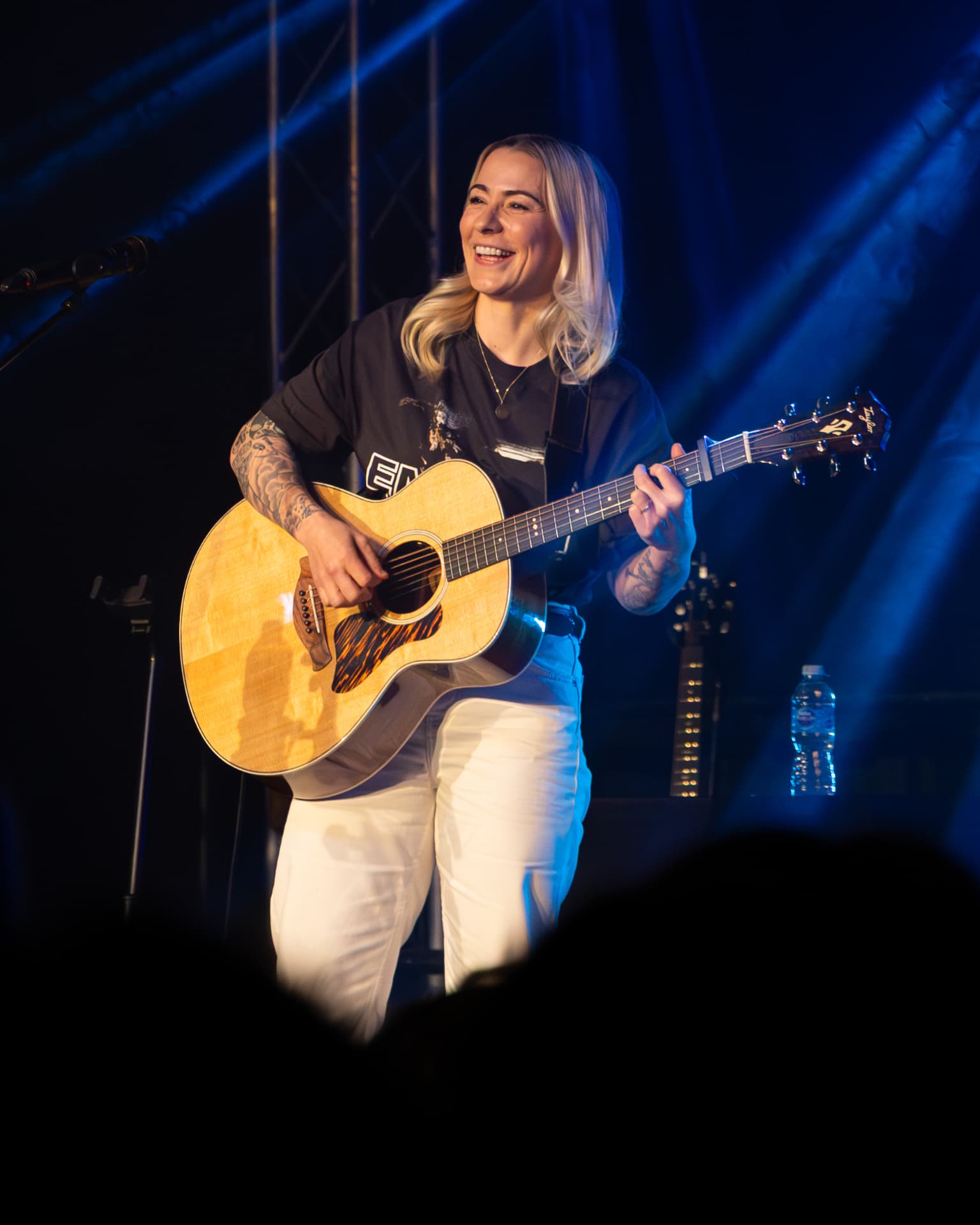 Full length on stage with acoustic guitar in blue light
