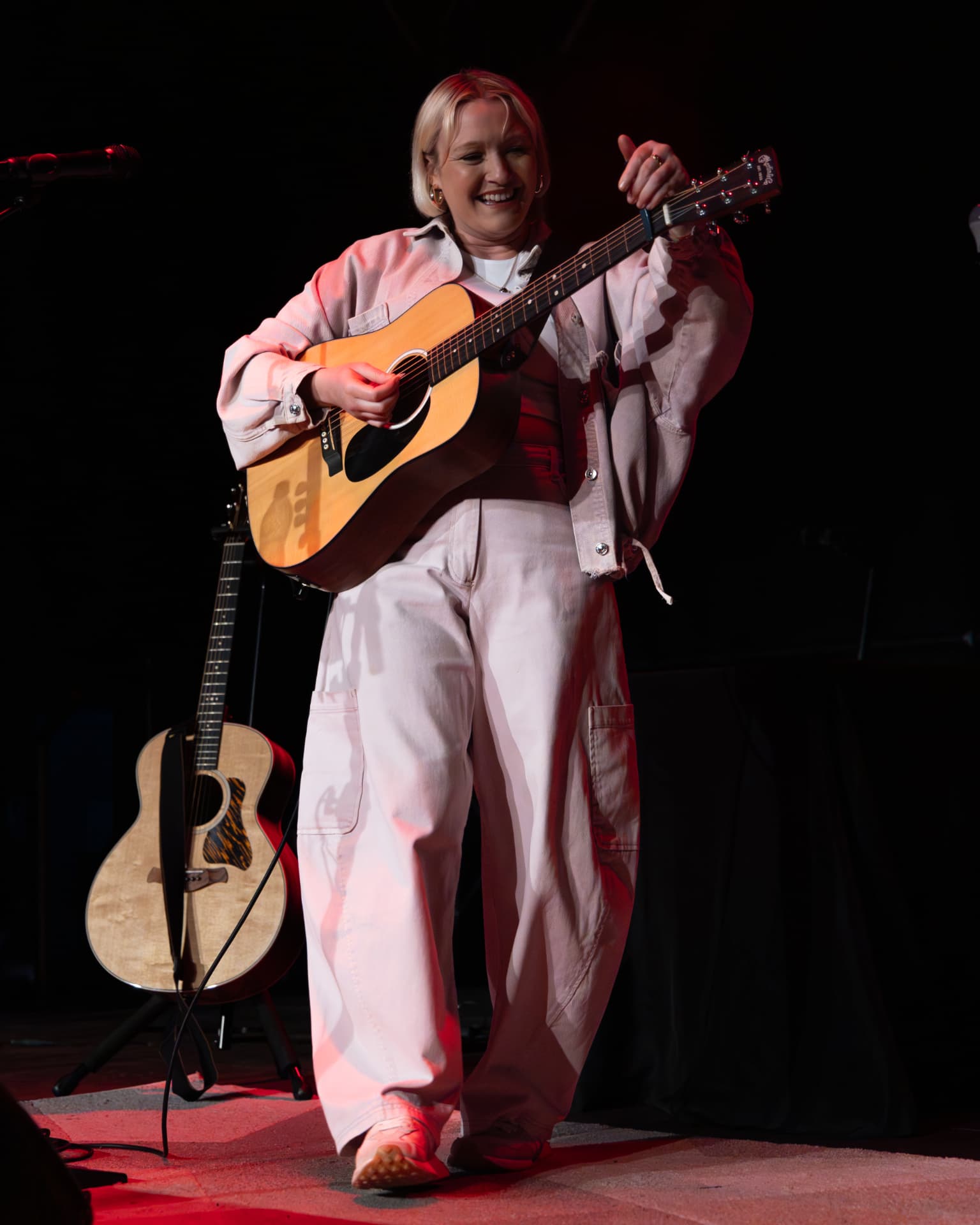 Molly Warburton performing with acoustic guitar on a red-lit stage