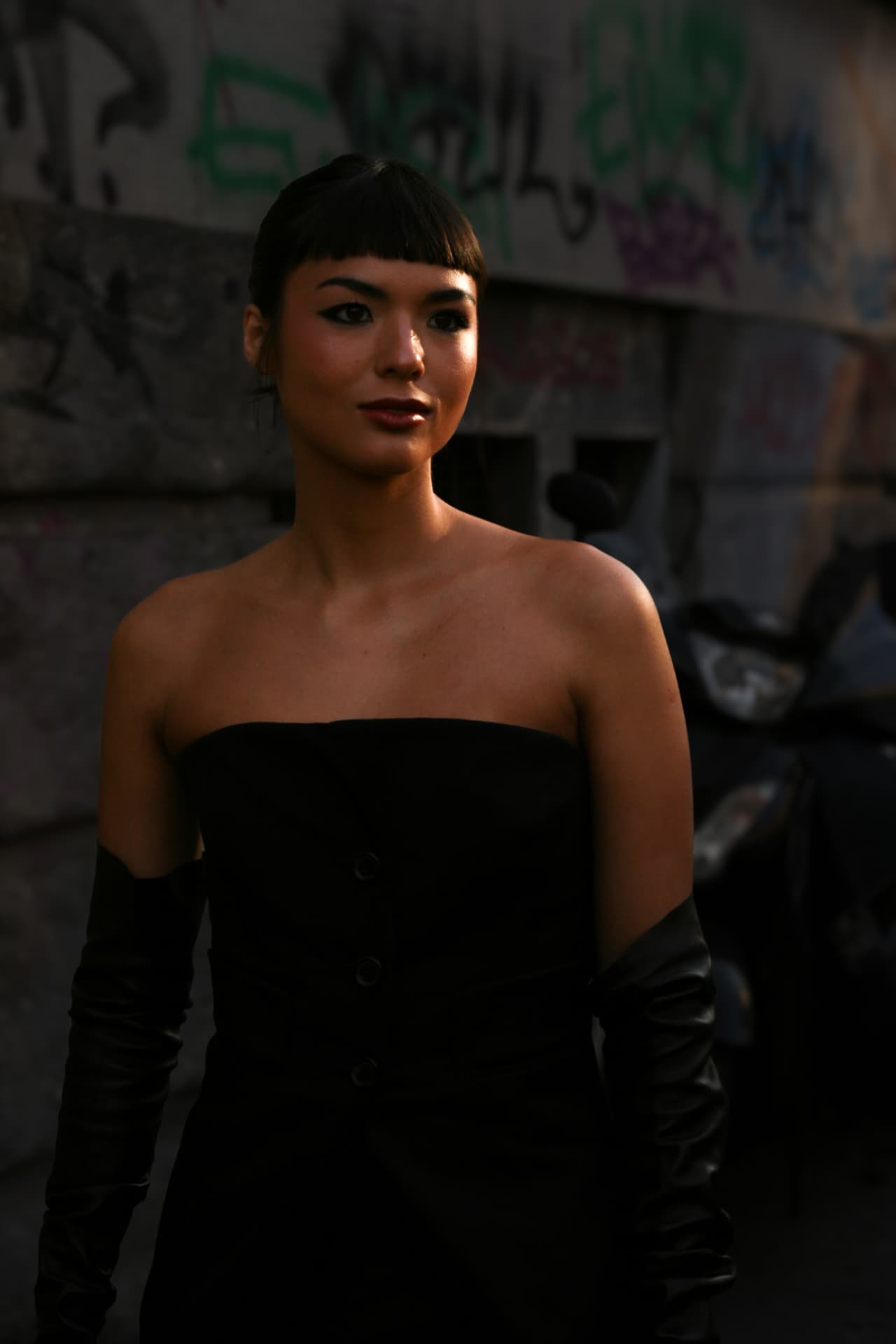 Guest in a black strapless dress and gloves in low light