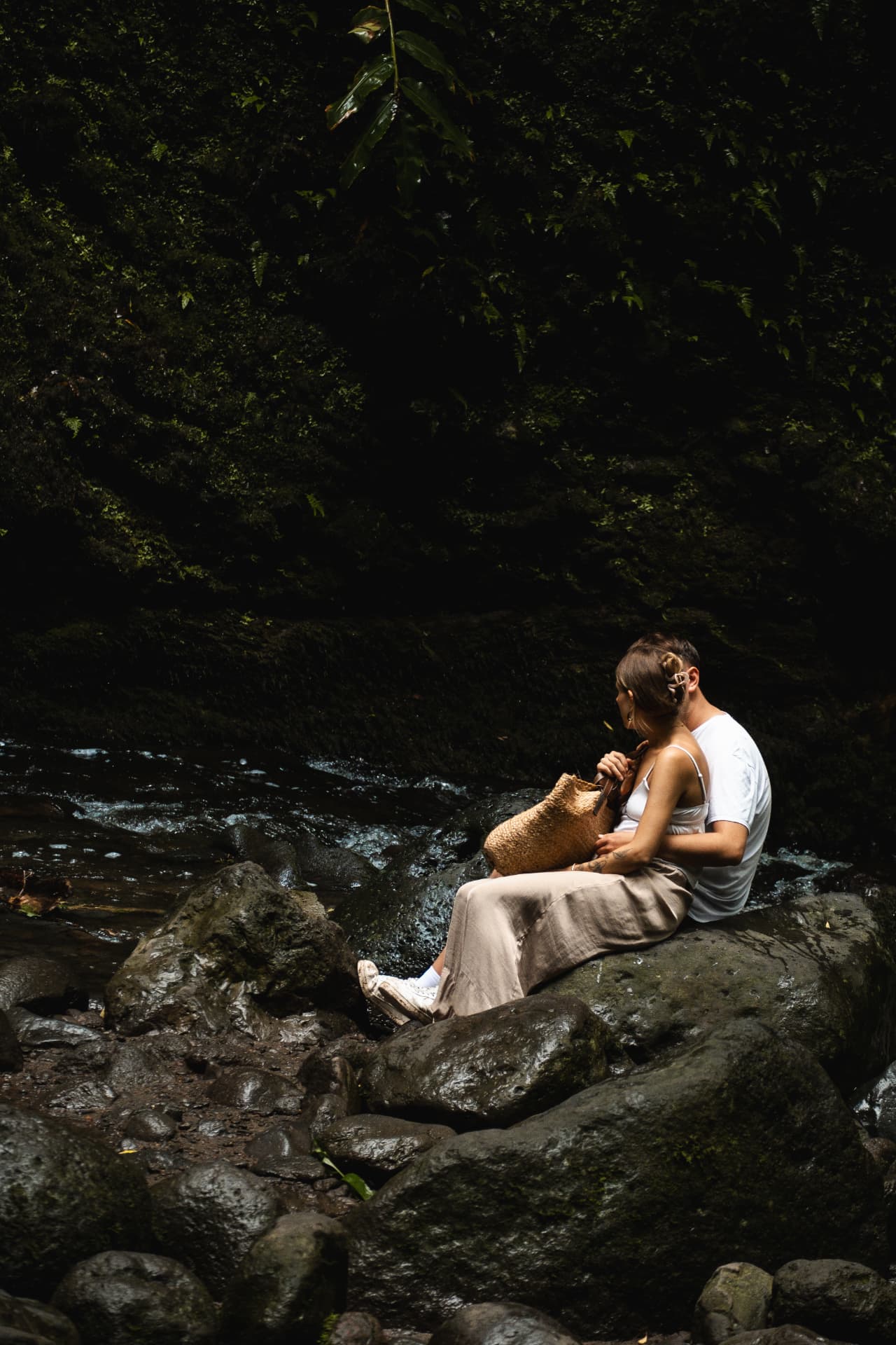 Couple sitting on rocks beside a forest stream