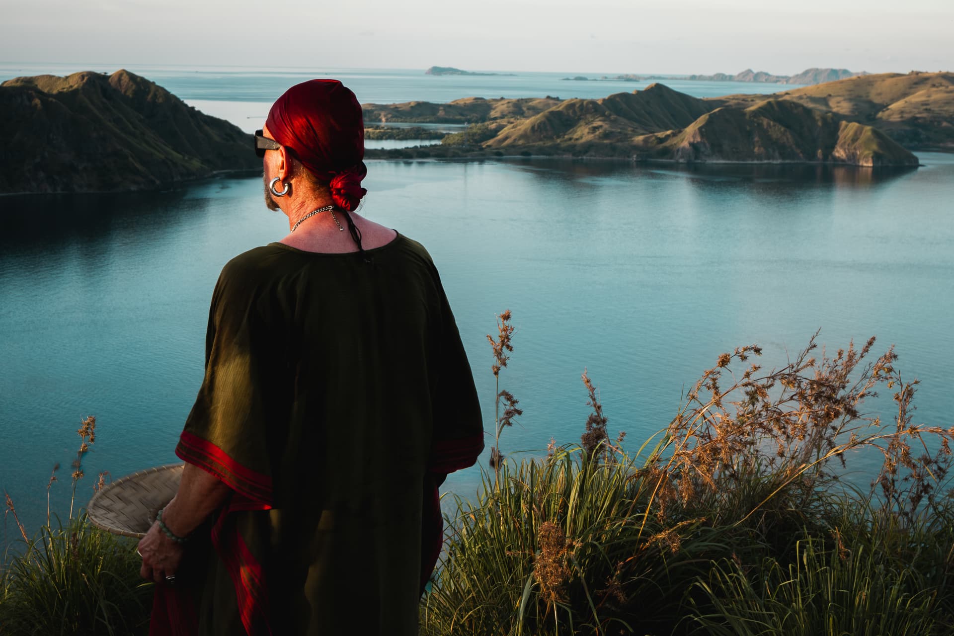 Figure in a red headscarf looking out over island-studded turquoise water