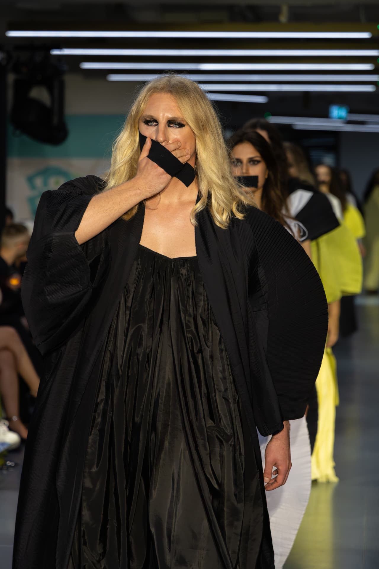 Model in a black draped gown with a taped mouth detail