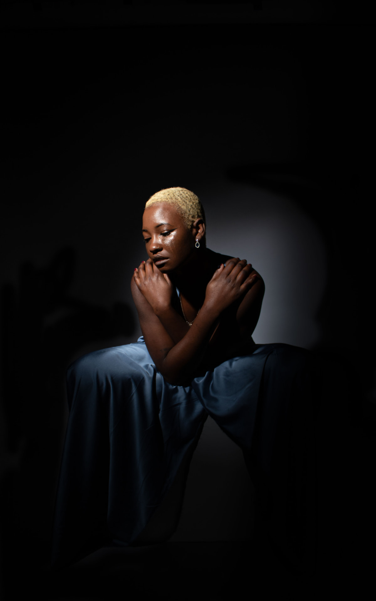Model seated in a blue satin gown under a spotlight